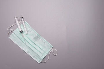 Syringes and medical face mask spread over grey background,flat lay angle