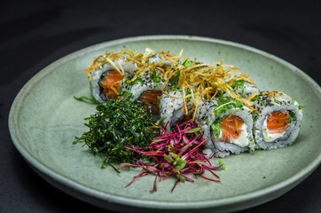 Sushi, traditional Japanese cuisine. Delicious Uramaki on decorated plate, black background.