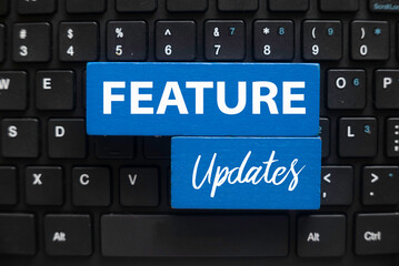 Top view of computer keyboard and blue wooden cube written with Feature Updates.