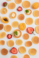 The pattern of small pancakes, fresh strawberries and apricots is laid out entirely. Background from orange toasts round pancakes. Trendy Food