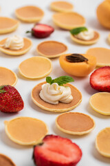 The pattern of small pancakes, fresh strawberries and apricots is laid out entirely. Background from orange toasts round pancakes. Trendy Food