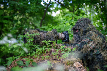 Fototapeta na wymiar Wildlife photographer in the summer ghillie camouflage suit