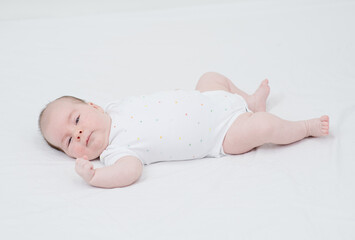 Two month old baby lies on the bed and looks at the camera