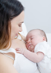 A newborn baby sleeps sweetly at mom's arms, mom looks at a sleeping baby with a smile