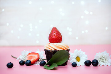 a small birthday cake with a large strawberry decorated with blueberries and flowers on a pink background