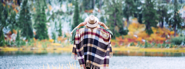 Adventure woman among mountains, enjoy the wild. Forest and lake wearing hat and poncho, boho and...