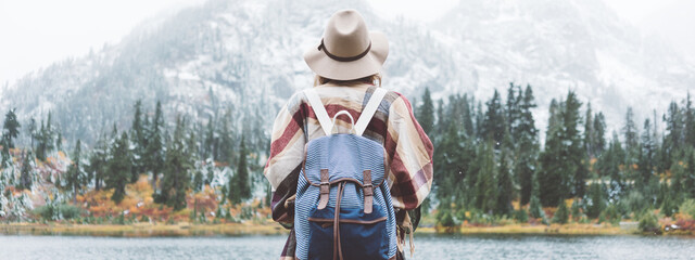 Styish woman feeling happy among amazing mountains, enjoy the nature landsape. Forest and lake, wearing backpack, hat and poncho, boho and wanderlust style. Wide screen, panoramic