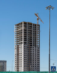 Fototapeta na wymiar Construction site with a multi-storey residential building under construction and a tower crane against a blue summer sky. Sterlitamak, Republic of Bashkortostan.