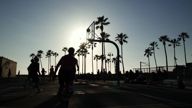 Young adult athletic players playing basketball in court in Venice Beach. Concept of urban sports, modern millennial active lifestyle & travel to Los Angeles, USA. Slow Motion.