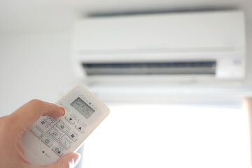 Man's hand using remote control open The air conditioner is cooled to 25 degrees Celsius in his bedroom. Health concepts and energy savings