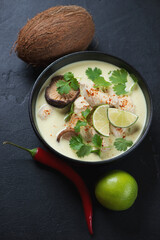 Bowl of thai traditional tom kha gai soup over black stone background, vertical shot