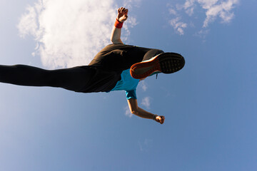 Fototapeta na wymiar Low angle view of a sportsman who jump and run with blue sky in background