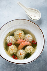 Bowl of wonton and shrimp soup over light-blue stone background, vertical shot, selective focus
