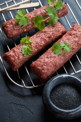 Raw kebabs made of marbled beef meat with fresh cilantro and black salt, close-up, vertical shot