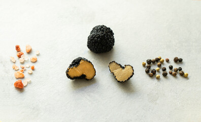 Black truffles, pink mineral salt and black pepper lie on a gray background. Freshly Sliced Truffle. Piquant and fragrant French delicacy. Close-up