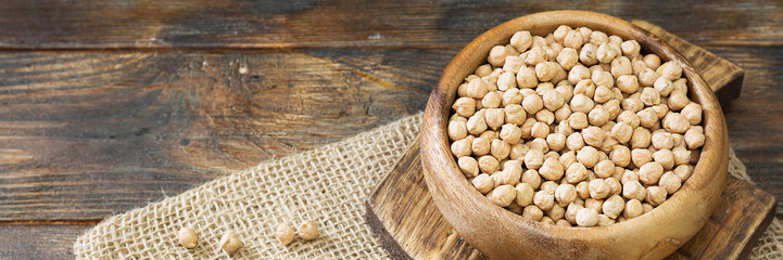 Chickpeas in a wooden bowl on the brown kitchen table. Raw chickpeas close-up. Banner with space for text