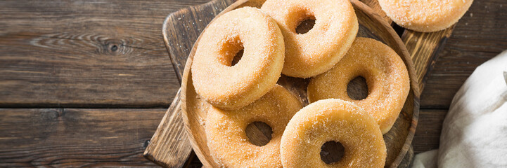 Doughnuts in sugar on a wooden Board on the brown kitchen table. Lots of doughnuts on the plate. Top view with space for text. banner