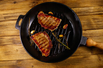Grilled pork steaks with rosemary, garlic and spices in cast iron grill frying pan on wooden table....