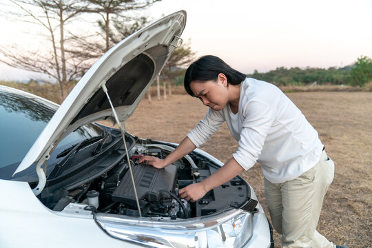 Asian man is stressed with the broblem car and try to fix it by himself in the large field forest behind.