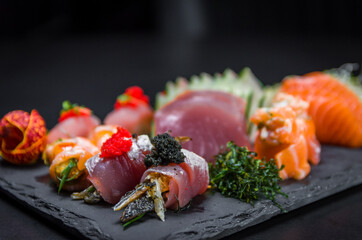 Sushi, traditional Japanese cuisine. Several delicious sushi on the decorated plate, black background. Group of sushi, Urakami, Nigori, Sushi jow, sashimi, tekamaki, etc ...