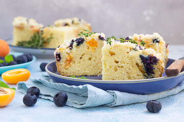 Slices of apricot and blueberry crumble cake on blue ceramic plate decorated with thyme. Blue...