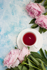 Cup of tea and pink peonies flowers on blue stone background. Top view with copy space for text. Present for Woman or Mother day.