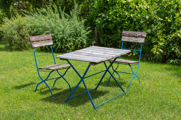 two metal chairs and a table in a garden surrounded by bushes