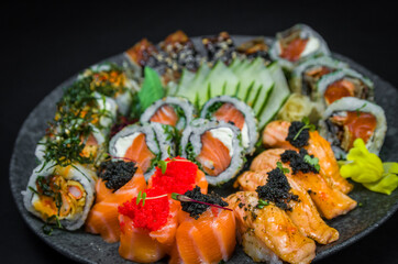 Sushi, traditional Japanese cuisine. Several delicious sushi on the decorated plate, black background. Group of sushi, Urakami, Nigori, Sushi jow, sashimi, tekamaki, etc ...