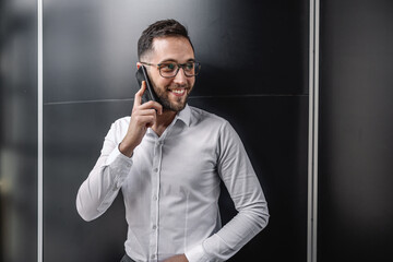 Cheerful smiling businessman standing indoors and using smart phone.