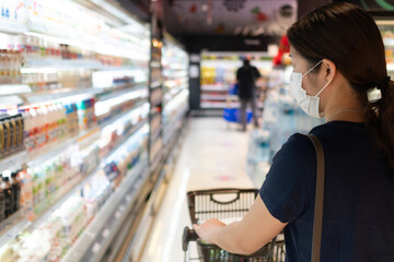 young asian woman wearing mask and keeping social distancing while shopping food in supermarket. new normal, covid-10 and coronavirus concept