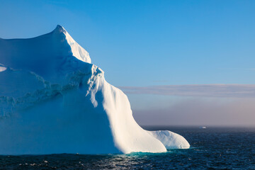 Huge floating iceberg, spectacular and beautiful, lit by violet evening light, with clearing mist, Bransfield Strait, near South Shetland Islands and Antarctic Peninsula, Antarctica