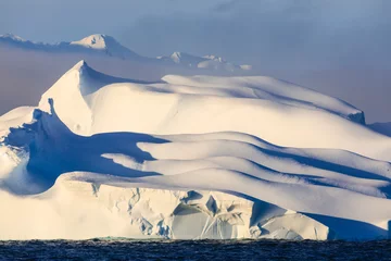 Fotografie eines riesigen goldenen eisigen antarktischen Eisbergs mit spektakulärer Tiefenschärfe, Eisschichten und -falten, lichtendem Nebel, entfernter Bergkette, Bransfield Strait, Polarregion, gefrorener Antarktis © Eleanor Scriven 
