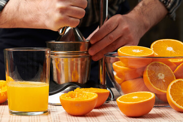 Squeezing an orange with a manual press, close view, making a glass of fresh. Fresh oranges on a wooden table, whole, squeezed and sliced.