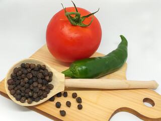 Closeup isolate: black pepper, juicy red tomato, green chili pepper. Fresh vegetables and spices on a wooden cutting board on a white background. Menu concept, ingredients for salad, healthy food.