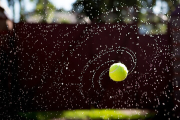 Wet Tennis ball photographed while flying and spinning at sunset on a warm summer evening....