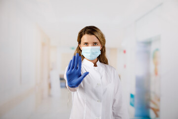 Female doctor in face mask showing stop sign with her hand
