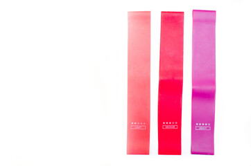 Elastic bands for fitness. Three elastic bands for fitness in close-up on a white background. Erasers lie on the table top and side view. A bunch of rezhinki, twisted into a roll. Elastic bands left 