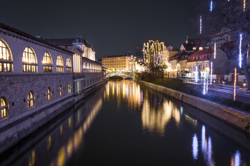 Night view of Ljubljanica River with famous Triple Bridge and medieval colorful buildings in Ljubljana, Slovenia. Reflection in water of Christmas lights in December. Long exposure, wide shot