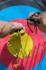 Vertical shot of two male hands pulling out arrows from an archery paper target.