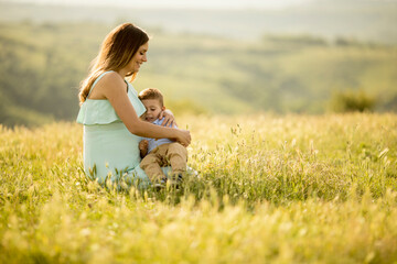 Fototapeta na wymiar Young pregnant mother with her cute little boy in the field on beautiful sunny day