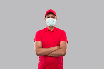 Delivery Man Standing Hands Crossed Wearing Medical Mask Isolated. Indian Delivery Boy in Red Uniform