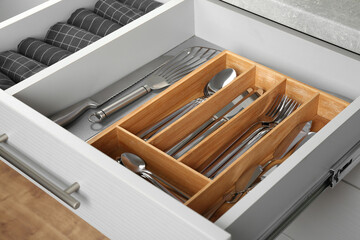 Open drawer with different utensils and folded towels. Order in kitchen