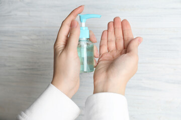 Woman applying antiseptic gel on hand against light background, above view