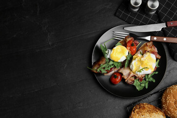 Delicious eggs Benedict served on black table, flat lay. Space for text