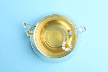 Delicious chamomile tea in glass cup on light blue background, top view