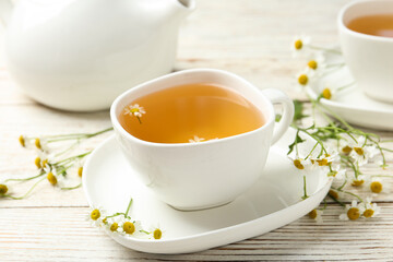 Cup of tea and chamomile flowers on white wooden table