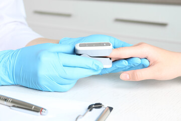 Doctor examining patient with fingertip pulse oximeter at white wooden table in office, closeup