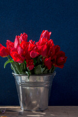 bucket of red tulips on a wooden table on a dark background