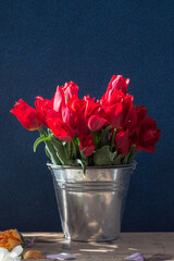 bucket of red tulips on a wooden table on a dark background