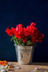 bucket of red tulips on a wooden table on a dark background